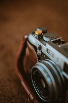 a camera sitting on top of a wooden table next to a brown leather case with buttons