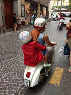 a man and woman riding on the back of a scooter down a street