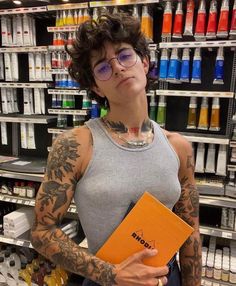 a woman with tattoos holding an orange folder in front of a store shelf filled with bottles