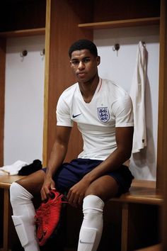 a young man sitting on top of a wooden bench in a locker room holding a soccer shoe