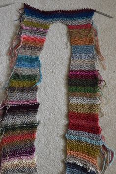 a multicolored knitted scarf laying on the floor next to a pair of scissors