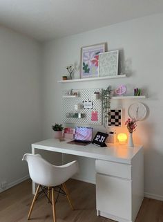 a white desk topped with a laptop computer next to a wall mounted shelf filled with pictures