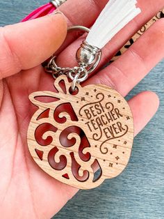 a hand holding a wooden keychain that says best teacher ever with an owl on it