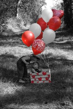 a little boy sitting in a box with red and white balloons