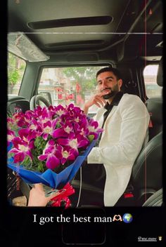 a man sitting in the back seat of a car holding a bouquet of purple flowers