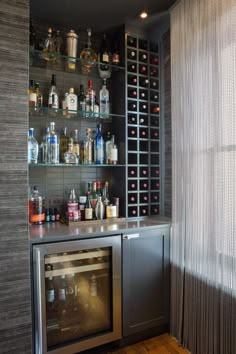 a bar with bottles on the shelves and wine glasses on the wall behind it in front of a window