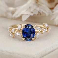 an oval blue sapphire surrounded by white and yellow gold leaves sits on a cushioned surface