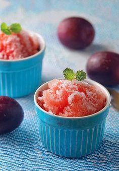 two blue bowls filled with ice cream next to plums on a tablecloth,