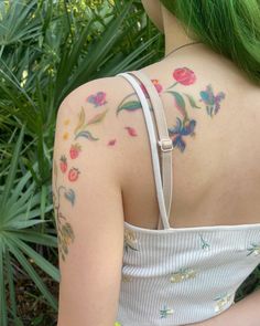 a woman with green hair and tattoos on her back is standing in front of some plants