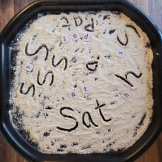 an uncooked pizza sitting on top of a black pan covered in letters and numbers