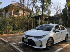 a white car parked in a parking lot next to some trees and bushes on the side of a house