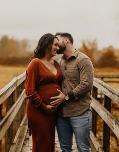 a pregnant couple standing on a bridge in an open field during their fall engagement session