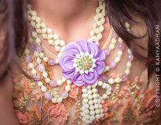 a close up of a woman wearing a necklace with flowers on it and pearls around the neck