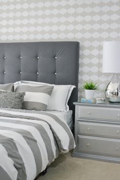 a bedroom with grey and white bedding, striped pillows and a gray headboard