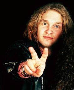 a man with long hair pointing at the camera while wearing a leather jacket and holding his finger up