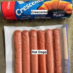 four hot dogs in plastic wrappers next to a can of crescent cremens