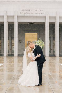 a bride and groom kissing in front of the courthouse building on a rainy day with snow falling all around them