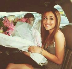 a beautiful young lady sitting in the back seat of a car holding a bouquet of flowers