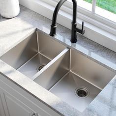 two stainless steel kitchen sinks with black faucets in front of a large window