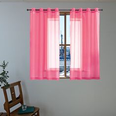 a pink curtain hanging from the side of a window next to a small wooden chair