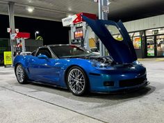 a blue sports car parked in front of a gas station with its hood up open