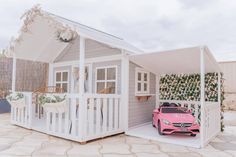 a pink toy car is parked in front of a white doll house with a porch