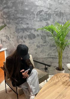 a woman sitting in a chair holding a cell phone next to a potted plant