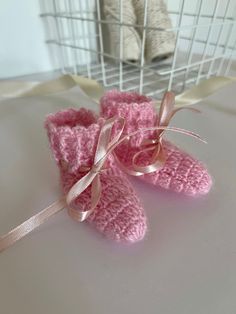 pink crocheted baby booties sitting on top of a white table next to a teddy bear