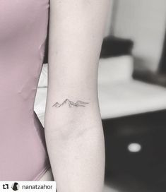 a woman's arm with a small mountain tattoo on the left side of her arm