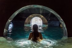 a woman is sitting in the middle of a swimming pool with an archway leading into it