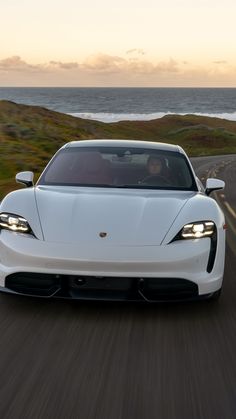 the white sports car is driving down the road near the ocean at sunset or dawn