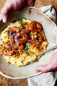 a person holding a spoon in a bowl filled with mashed potatoes, shrimp and corn