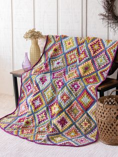 a crocheted granny blanket sitting on top of a wooden bench next to a basket