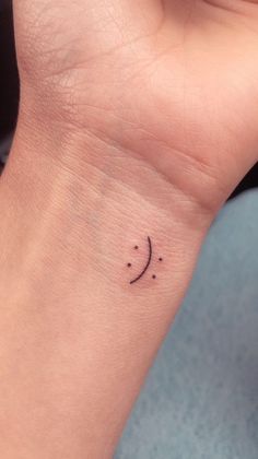 a small wrist tattoo with a smiley face on the left side of the wrist and dots in the middle