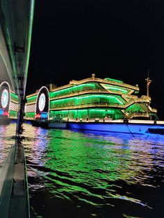 a large building lit up with green lights on it's sides next to the water