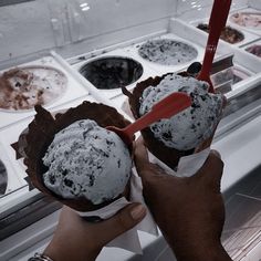 two people holding up ice cream in front of an open freezer filled with different types of desserts