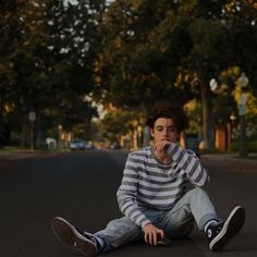 a young man sitting on the ground with his hand to his mouth and looking at the camera