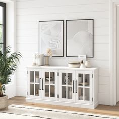 a white cabinet with two pictures on the wall and a potted plant next to it