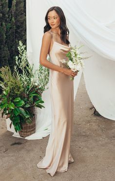 a woman standing in front of a white backdrop holding a flower pot with greenery