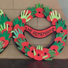 two handprinted wreaths with red flowers and green leaves are on a brick wall