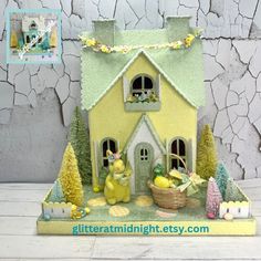 there is a small yellow house with trees and eggs in the front, on a table