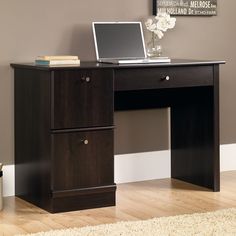 a desk with a laptop on top of it in front of a wall and rug