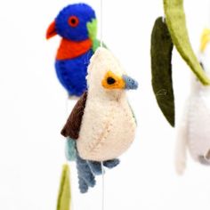 three colorful birds hanging from strings on a white wall with green leaves and one blue bird in the foreground