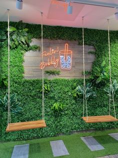 two wooden swings hanging from the side of a green wall with plants growing on it