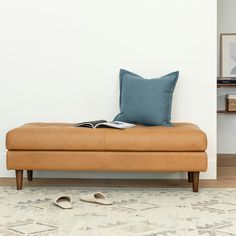 a tan bench with a book and slippers on it in front of a white wall