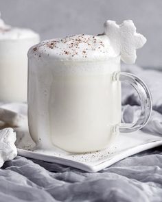 two mugs with marshmallow and whipped cream on them sitting on a white plate