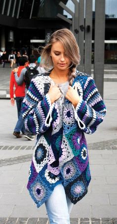 a woman is walking down the street wearing a crocheted jacket