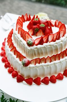 a three layer cake with strawberries and cream frosting on the top is sitting on a table