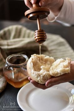 a person pouring honey into a bun on a plate