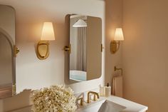 a white sink sitting under a bathroom mirror next to a vase with flowers on it